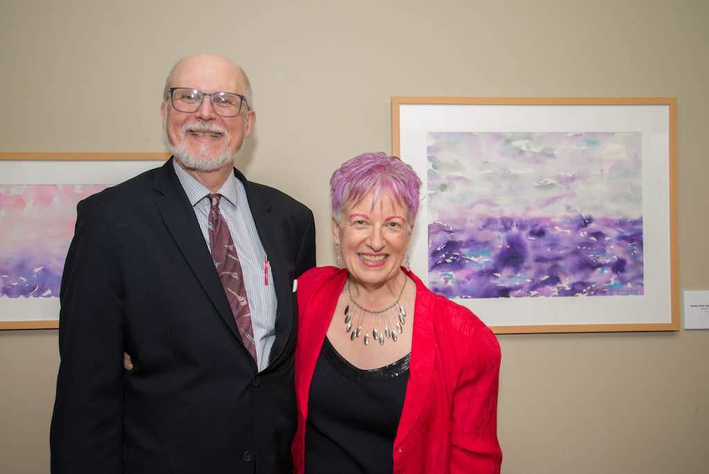 Anne and Bill in front of her watercolor paintings at art exhibition