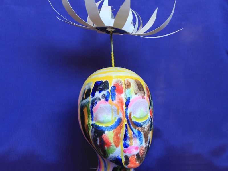 Colorful painted portrait sculpture with paper petaled flower floating above head